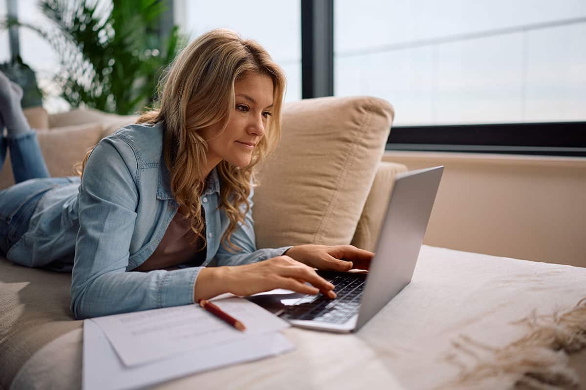 mid-adult-woman-working-computer-while-relaxing-sofa make money online, woman working on her laptop on the sofa
